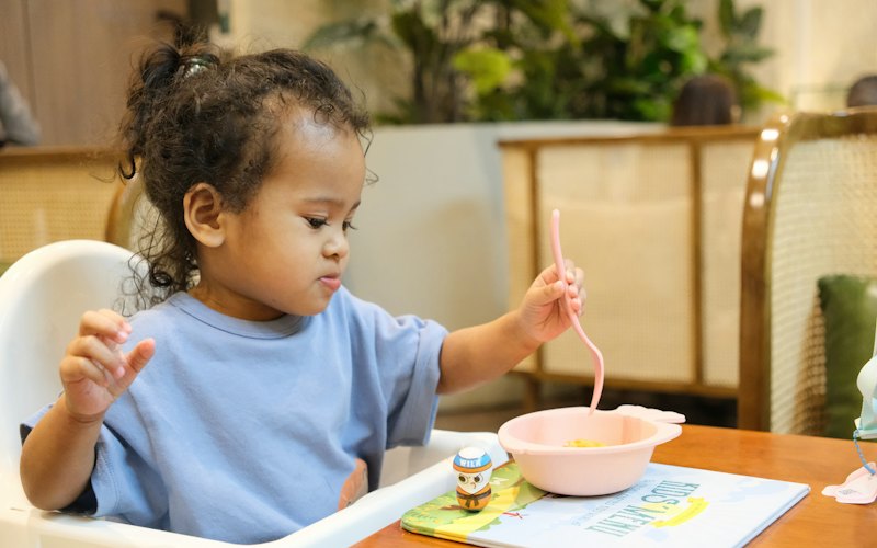 A toddler eating from a bowl with a spoon at the table