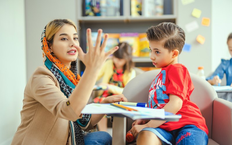 A therapist using hand gestures to help a young boy with speech practice